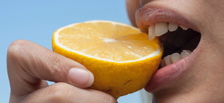 Close up of mouth with teeth biting into half on orange, against light blue sky