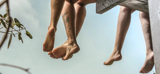 Feet dangling off edge of wooden platform outside in open air with trees nearby