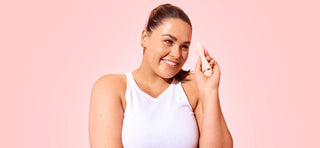 Woman with brown hair and white singlet smiling while holding VUSH Rose 2 bullet vibrator